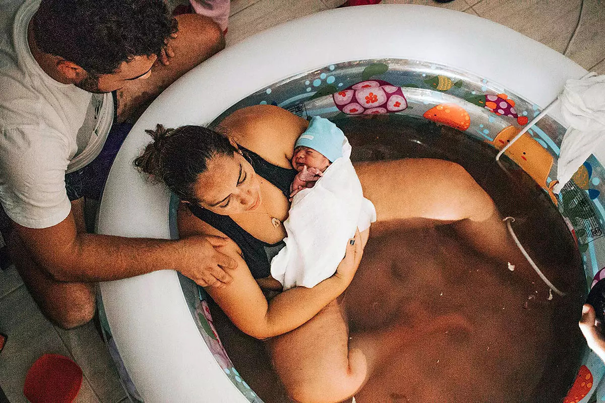 A mother holding her newborn in a birth tub, illustrating how natural birth supports early breastfeeding water birth experience showing immediate skin-to-skin contact for successful breastfeeding initiation
